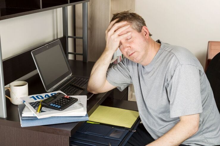 Uomo con mano sulla fronte, stressato davanti al PC con calcolatrice