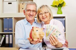 Coppia di pensionati: lui con salvadanaio maialino e lei con banconote euro, felici