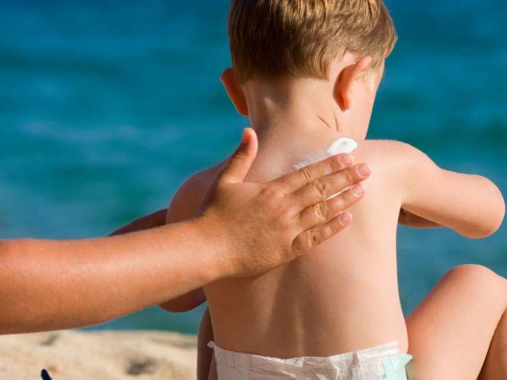 Mano che mette crema solare su bambino