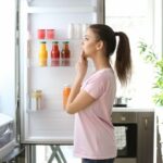 Ragazza guarda nel frigo con sportello aperto
