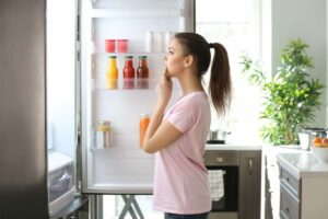Ragazza guarda nel frigo con sportello aperto