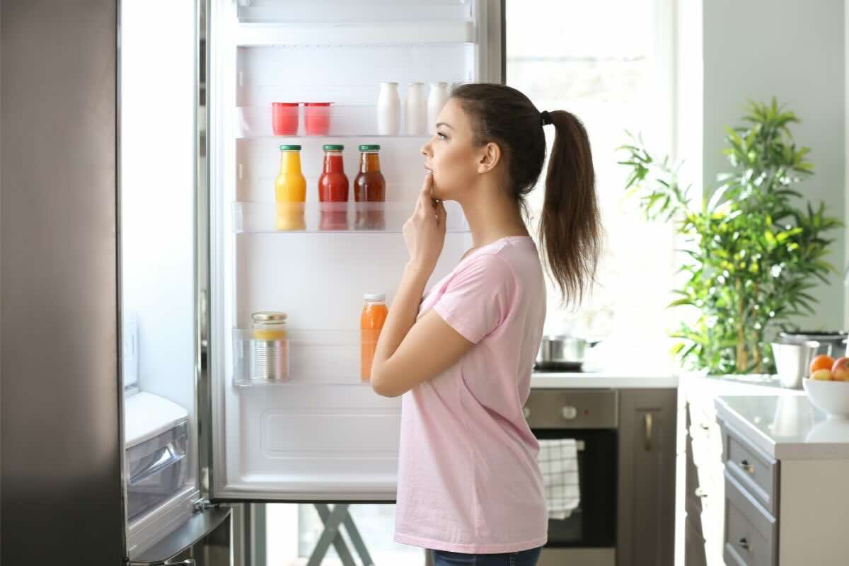 Ragazza guarda nel frigo con sportello aperto