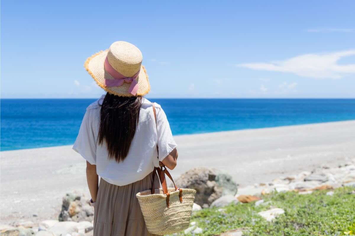 Donna con cappello di paglia, borsa, vestita al mare