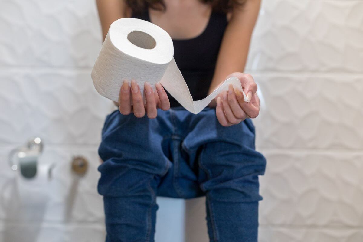 Ragazza seduta sul WC con rotolo carta igienica