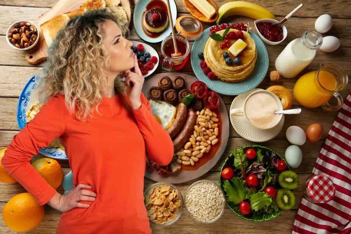 Ragazza pensa indecisa e sullo sfondo tanti piatti per la colazione dolce o salata